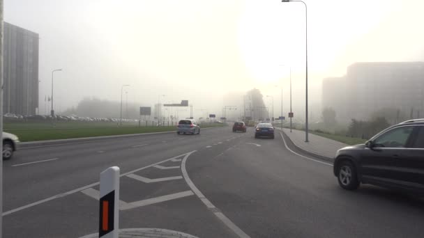 Os carros dirigem através da rua e a luz do sol penetra através do nevoeiro enorme. 4K — Vídeo de Stock