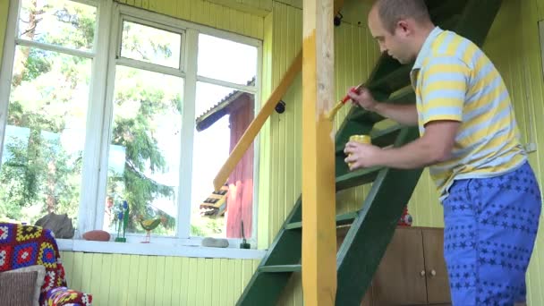 Hombre pintar columna de madera de color amarillo cerca de escaleras a loft. 4K — Vídeo de stock