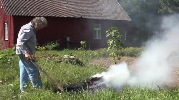 Жінка-старший садівник спалює траву і відмовляється від вогню на лузі в сільському дворі сільського будинку. 4-кілометровий — стокове відео