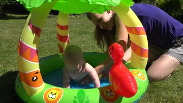 Bambina nuotare in piscina di acqua di gomma nel parco. La mamma tiene il bambino. 4K — Video Stock