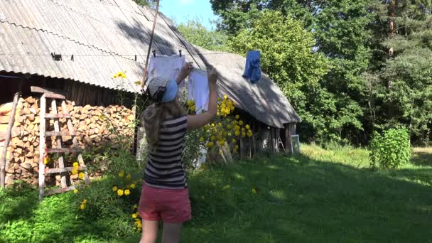 Chudé země žena dívka věší prádlo ručník na prádelní šňůru řetězec venkovský dům dvoře. 4k — Stock video