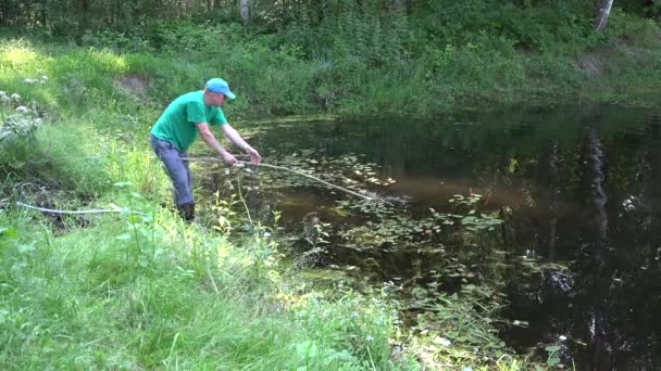 Людина очищається з граблями трави і крутішим сільським ставком літнього часу. 4-кілометровий — стокове відео