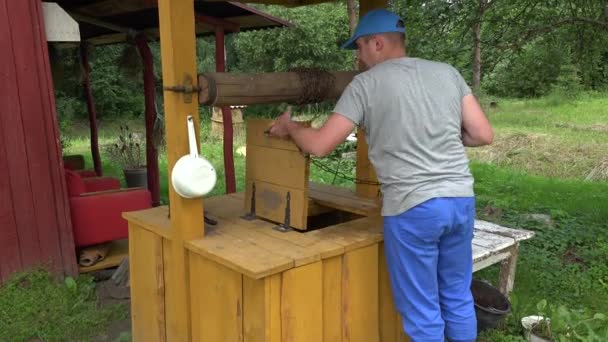 Hombre cae cadena con cubo en pozo rústico para sacar agua. 4K — Vídeo de stock