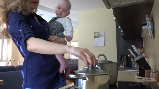 Woman with baby in hands cooking mix meal in pot and taste. 4K — Stock Video