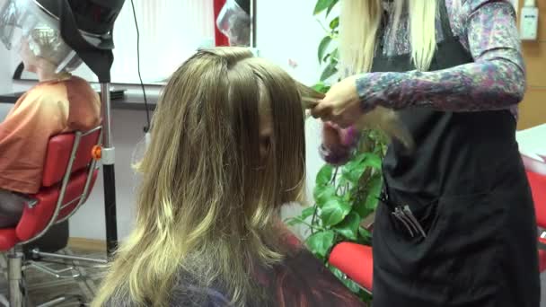 Hairdresser do haircut for female with long hair and woman under hair dryer. 4K — Stock Video