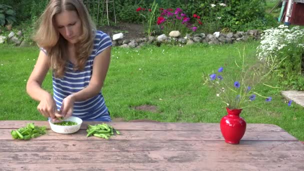 Villager chica rubia vaina verde guisantes sanos en la mesa de madera. 4K — Vídeo de stock