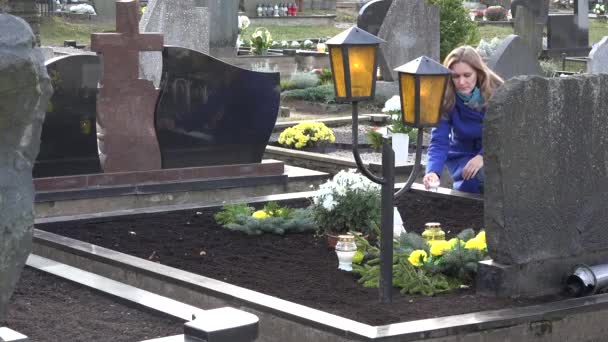 悲しい女性は、墓地に愛する父の兄の墓にろうそくを置きます。4 k — ストック動画