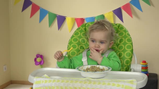 Roliga barn girl äta mosar med sked och händer sitter i baby utfodring stol. — Stockvideo