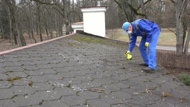 Man met beschermende kleren en gasmasker spray Moss met chemicaliën op het dak. — Stockvideo
