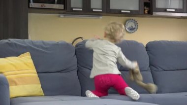 Young mother play hide and seek under sofa with her cute toddler daughter.