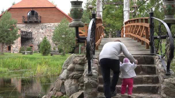 El hombre enseña al bebé a caminar sobre escaleras de piedra y puente de madera sobre el río. 4K — Vídeo de stock