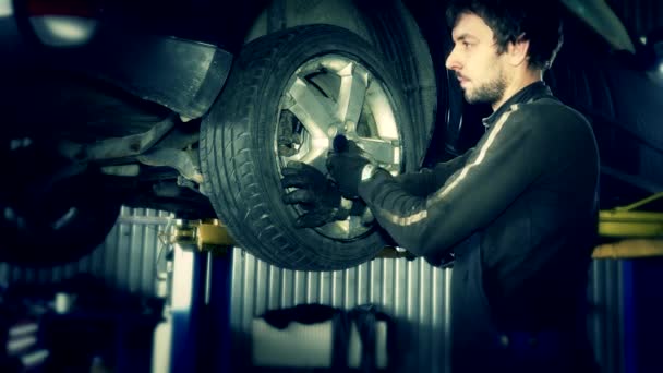 Mechaniker montiert Rad an Auto, das am Aufzug hängt. — Stockvideo