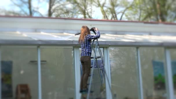 Vrouw schoonmaken glazen huis dak met hogedruk gereedschap in de natuur. — Stockvideo