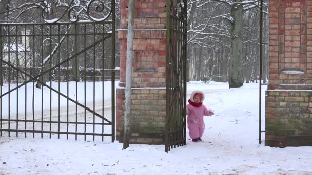 冬の雪に覆われたレトロな公園ゲートを通じて全体的な徒歩でのかわいい女の子。4 k — ストック動画