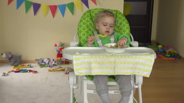 Peuter jongen eten mash met lepel zit in kinderstoel hoge voeding — Stockvideo