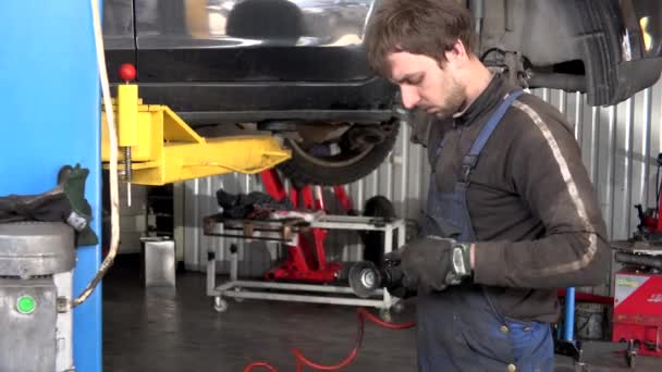 Mekanisk arbetare man grind rostiga bultar med elektrisk slipmaskin verktyg nära lyfte bilen — Stockvideo