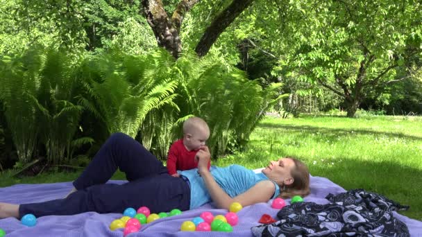 A mãe feliz põe-se na planície com a filha de bebê na planície no parque de verão. 4K — Vídeo de Stock