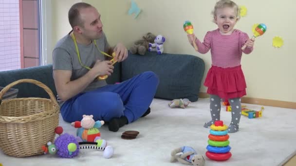 Vater spielt Spielzeuggitarre und kleine Tochter schüttelt Rassel. — Stockvideo