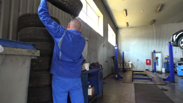 Pila de neumáticos y mecánico masculino tomar uno. Cambio de neumáticos de temporada en el garaje — Vídeo de stock