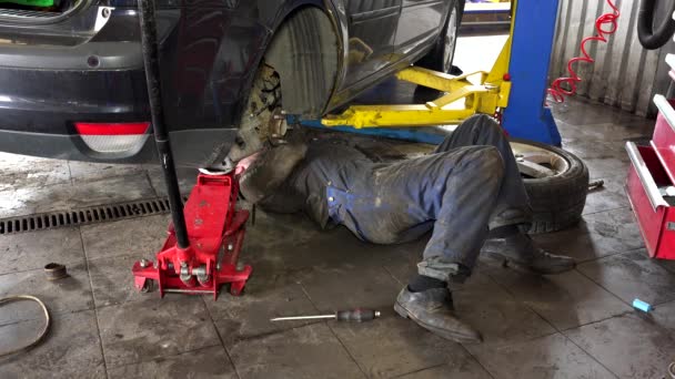 Mecânico deitado e trabalhando sob carro na garagem de reparação — Vídeo de Stock