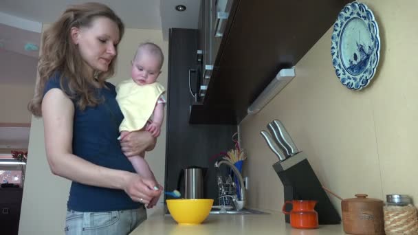 Mother hold her baby daughter and feed with spoon in kitchen. 4K — Stock Video