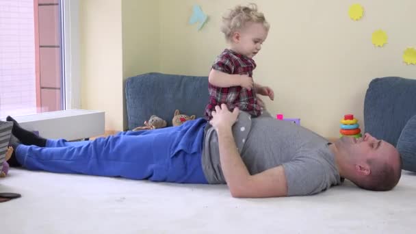 Schönes kleines Mädchen sitzt auf Papas Bauch und umarmt liebevollen Vater. — Stockvideo