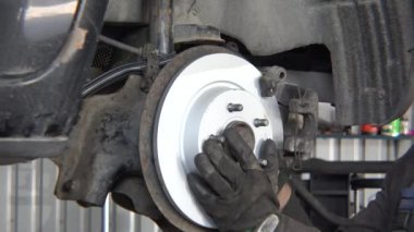 worker man mounting new brake disk on old car lifted in repair shop.
