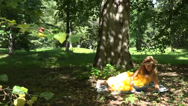 Mujer acostada en cuadros y leyendo libros en el parque en el hermoso día de verano soleado. 4K — Vídeos de Stock