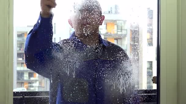 Hombre más limpio en aerosol uniforme azul y limpie la ventana con la herramienta limpiaparabrisas. — Vídeo de stock