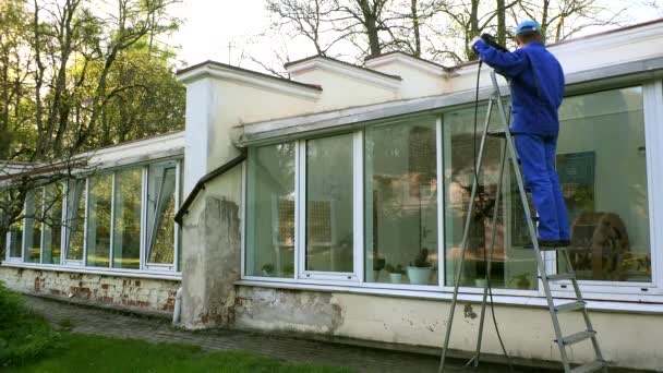 Muž na žebříku s vysokotlakého mytí nástroj čisté skleníku v přírodě. — Stock video