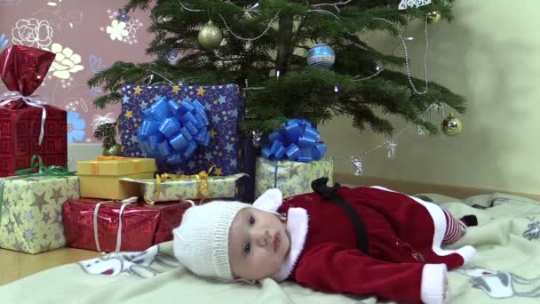 Bonito bebê menina mentira perto de árvore de natal e presente caixas — Vídeo de Stock