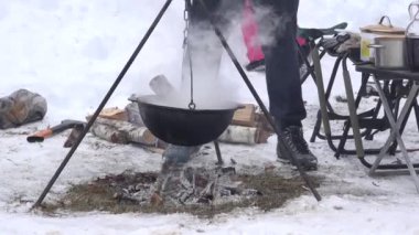 Turist insanlar kışın kamp ateşi ateşin üzerinde asılı tencerede pişirin. 4k
