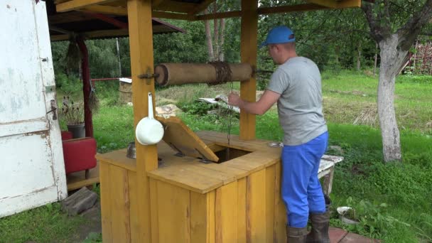 Садівник чоловік тягне воду з колодязя і закриває дерев'яні двері. 4-кілометровий — стокове відео