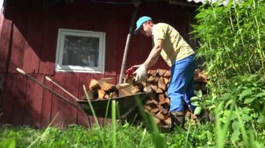 Çiftlik işçisi adam çocuğu yakacak odun ahşap paslı barrow sepeti boşalt. 4k