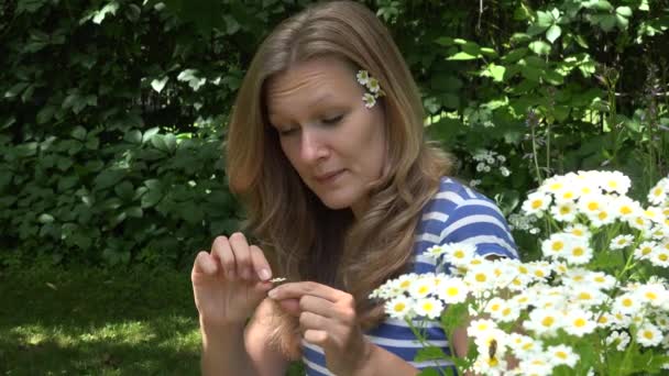 Jong meisje scheuren daisy bloemblaadjes in groen park. 4k — Stockvideo