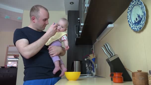 Happy father man feed baby son with spoon in kitchen. 4K — Stock Video