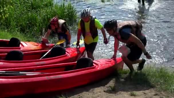 Deportistas con cascos protectores transportan canoas fuera del agua del río . — Vídeos de Stock