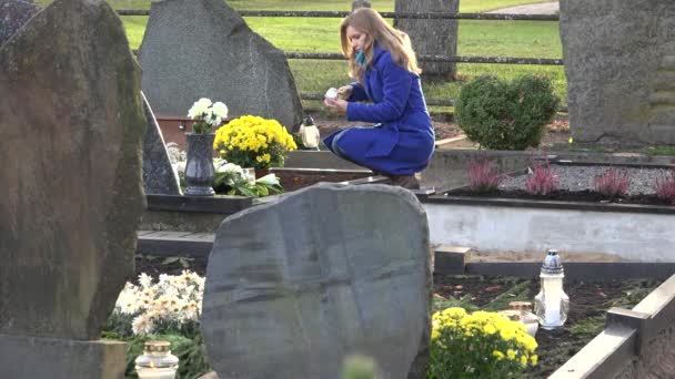 Молодая женщина зажигает свечу в память об отце-муже на кладбище. 4K — стоковое видео