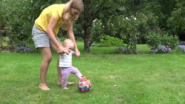 Giovane madre gioca con la bambina con la palla nel giardino estivo. 4K — Video Stock