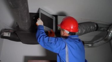 Kasklı teknisyen havalandırma düzenleyici filtrelerini kontrol ediyor.