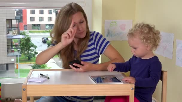 Busy mother on phone and baby use tablet in children room. 4K — Stock Video