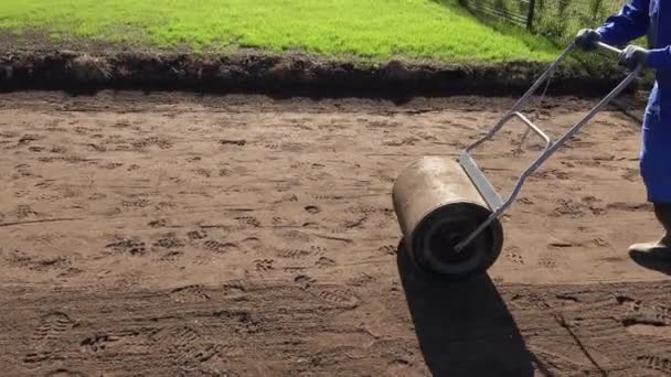 Arbetare drar gräsmattan roller för platta trädgården. Landskap på trädgård på våren — Stockvideo