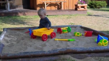 2 yaşındaki çocuk yazın kum havuzunda renkli oyuncaklarla oynuyor.