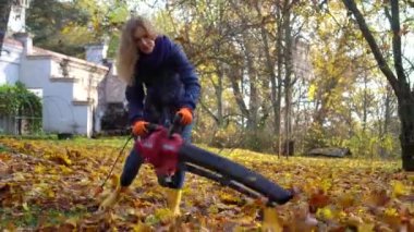 Skilled landscaper woman blowing leaves with leaf blower in customer house yard