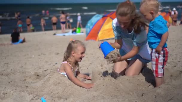 Мати з сином і дочкою грають на пляжному піску. Щаслива сім'я розважається на морі — стокове відео