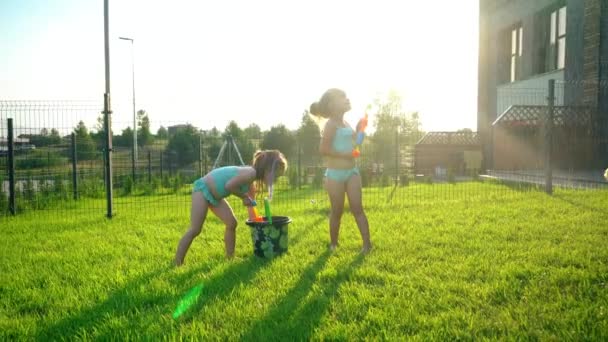 Genç kızlar su tabancasıyla su sıçratmaca oynuyorlar. Akşam güneşinde oyuncaklar. — Stok video