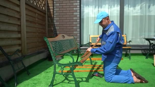 Homem trabalhando montar bancada pranchas de madeira. Trabalhador no desgaste do trabalho no gramado artificial — Vídeo de Stock