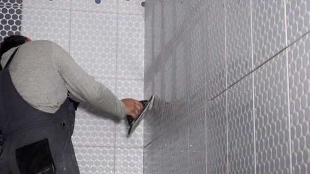 Tiler man filling gaps between tiles with grout using soft rubber trowel — Wideo stockowe