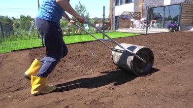 Female Townhouse Owner Compacts Soil With Hand Metal Roller. Gimbal shot