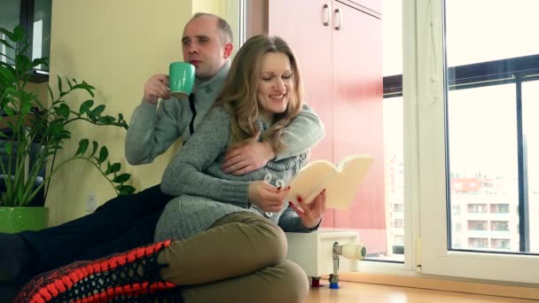 Paar liest Buch und trinkt Tee sitzen Heizkörper im Wohnzimmer. 4K — Stockvideo